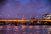 An iconic red bus drives over the Thames at dusk